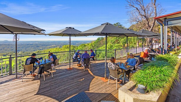 Um terraço com mesas, cadeiras, guarda-sóis e vista para a paisagem.