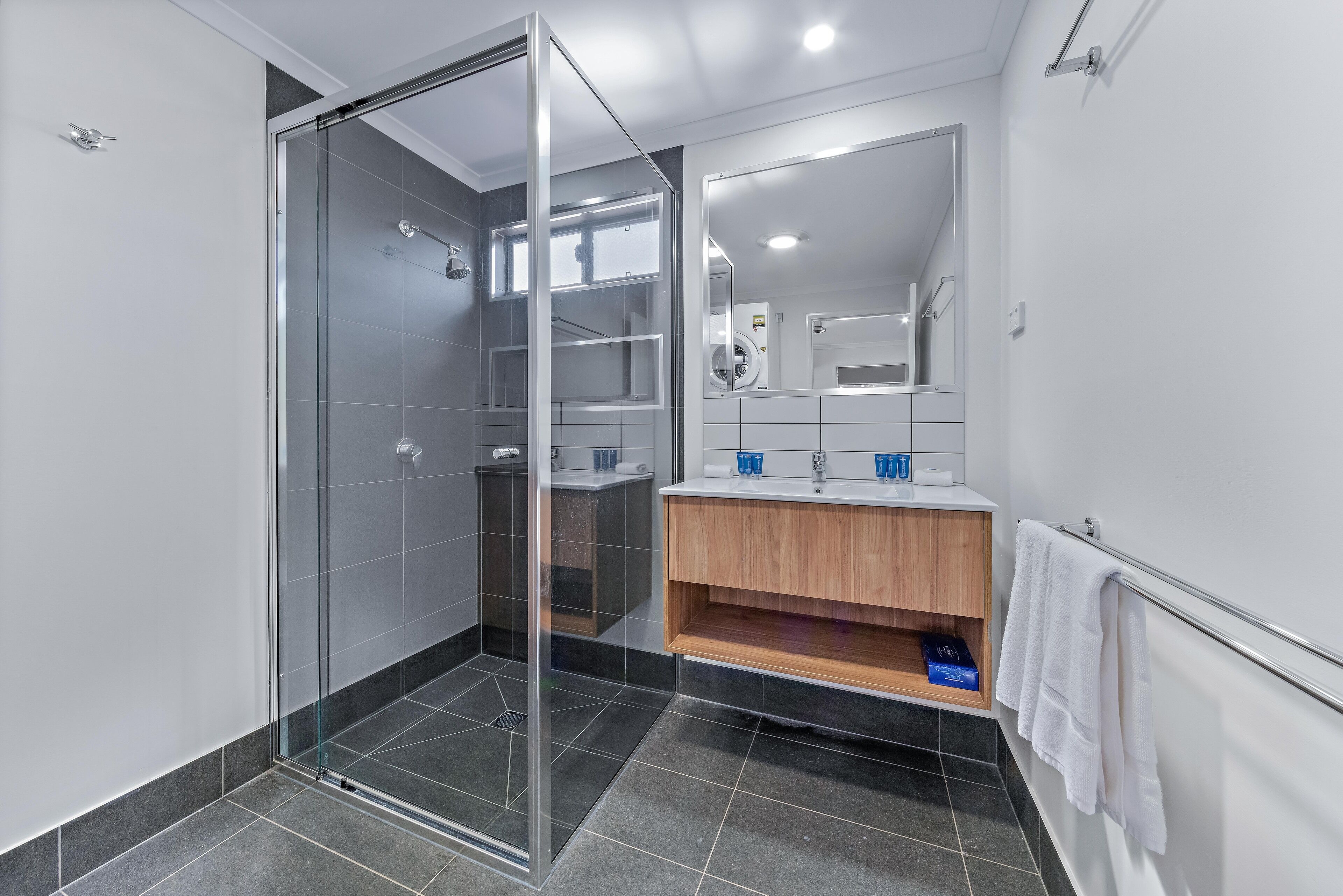 Un baño moderno con ducha de vidrio, tocador de madera y un espejo grande.