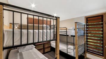 A bunk bed room with a wooden ladder, a small seating area with a cushion, and a window with blinds.