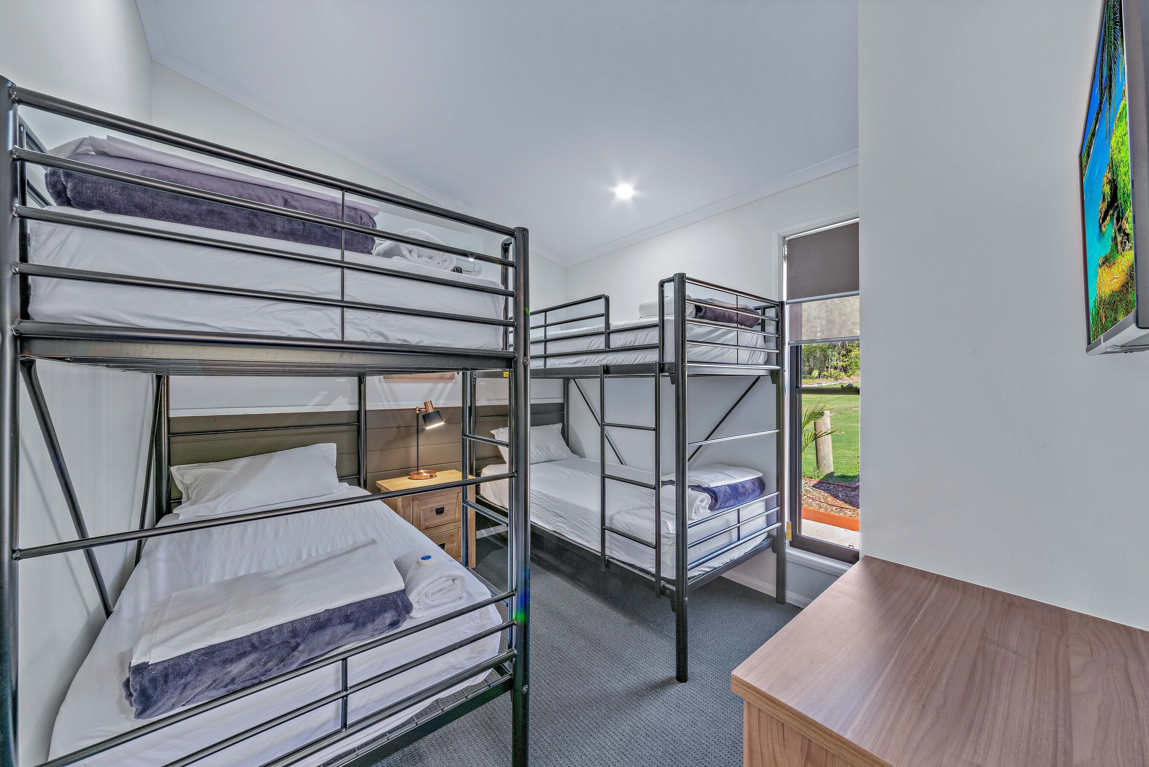 A dormitory room with bunk beds, a desk, and a window with a view of the outdoors.