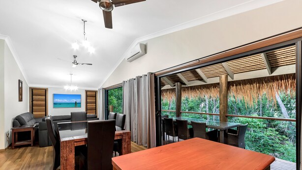 Sala de estar moderna com área de jantar, janelas amplas, ventiladores de teto e vista para o verde.
