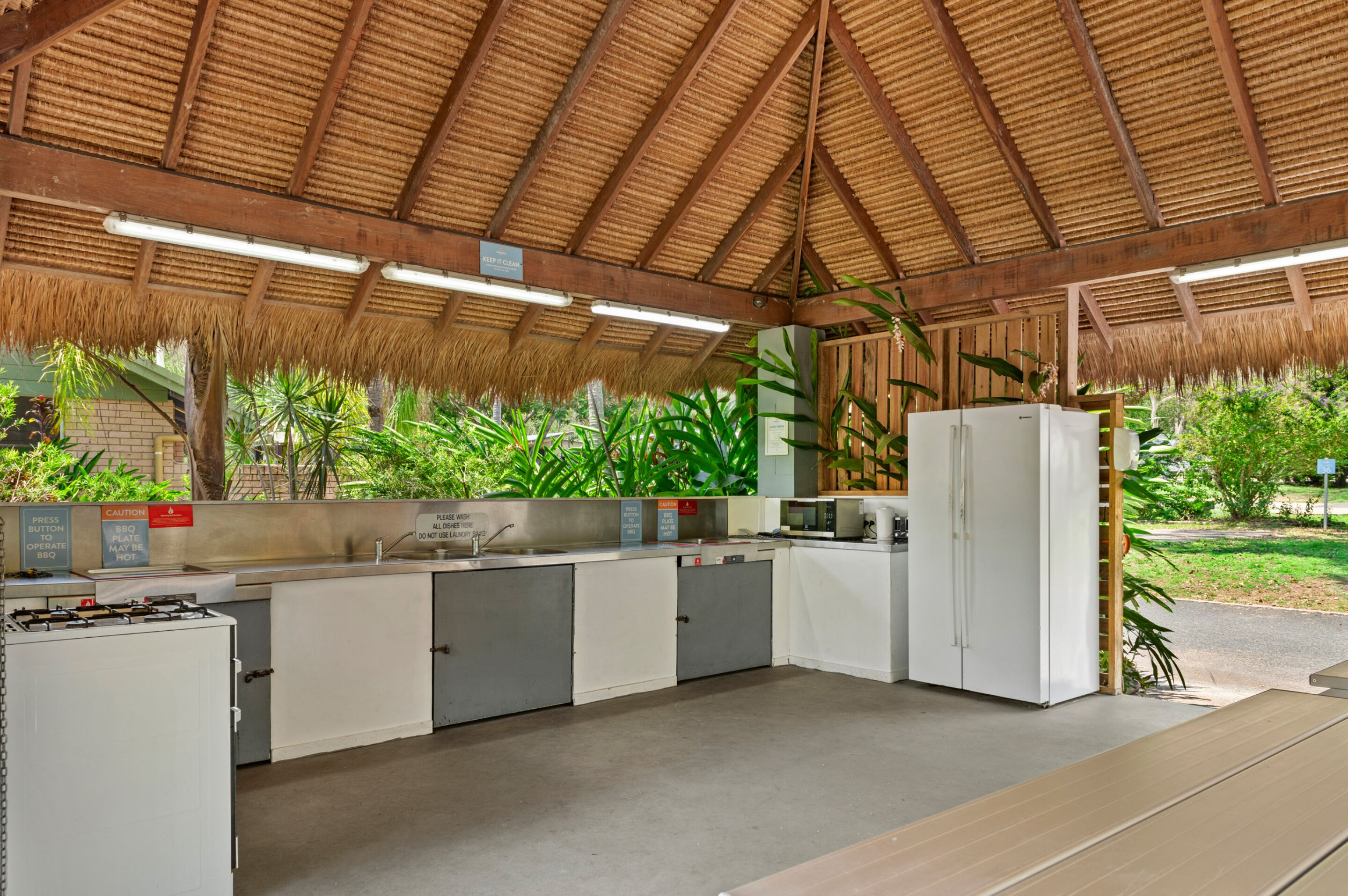 Une cuisine dotée d’un toit de chaume, d’appareils électroménagers intégrés et offrant une vue sur la verdure environnante.