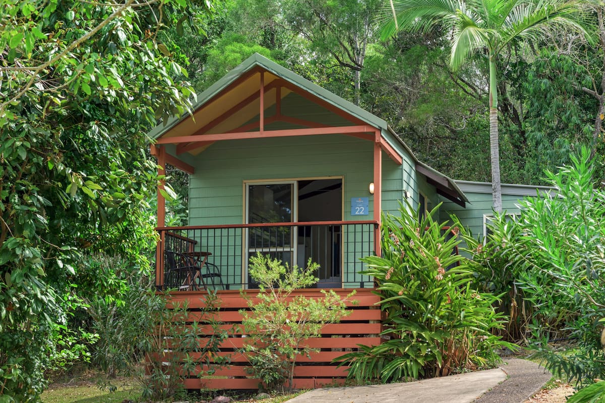 Ein kleines, eingeschossiges Haus mit Veranda, umgeben von üppiger Vegetation.