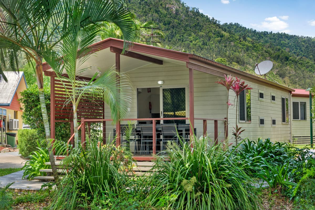 Ein Haus mit einer Veranda, umgeben von üppiger Vegetation und einer Berglandschaft im Hintergrund.