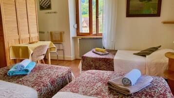 Une chambre avec deux lits, une table, une chaise et une fenêtre donnant sur des maisons.