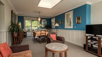 A living room with a blue wall, a dining area with a table and chairs, a sofa, a coffee table, and a television on a wooden stand.