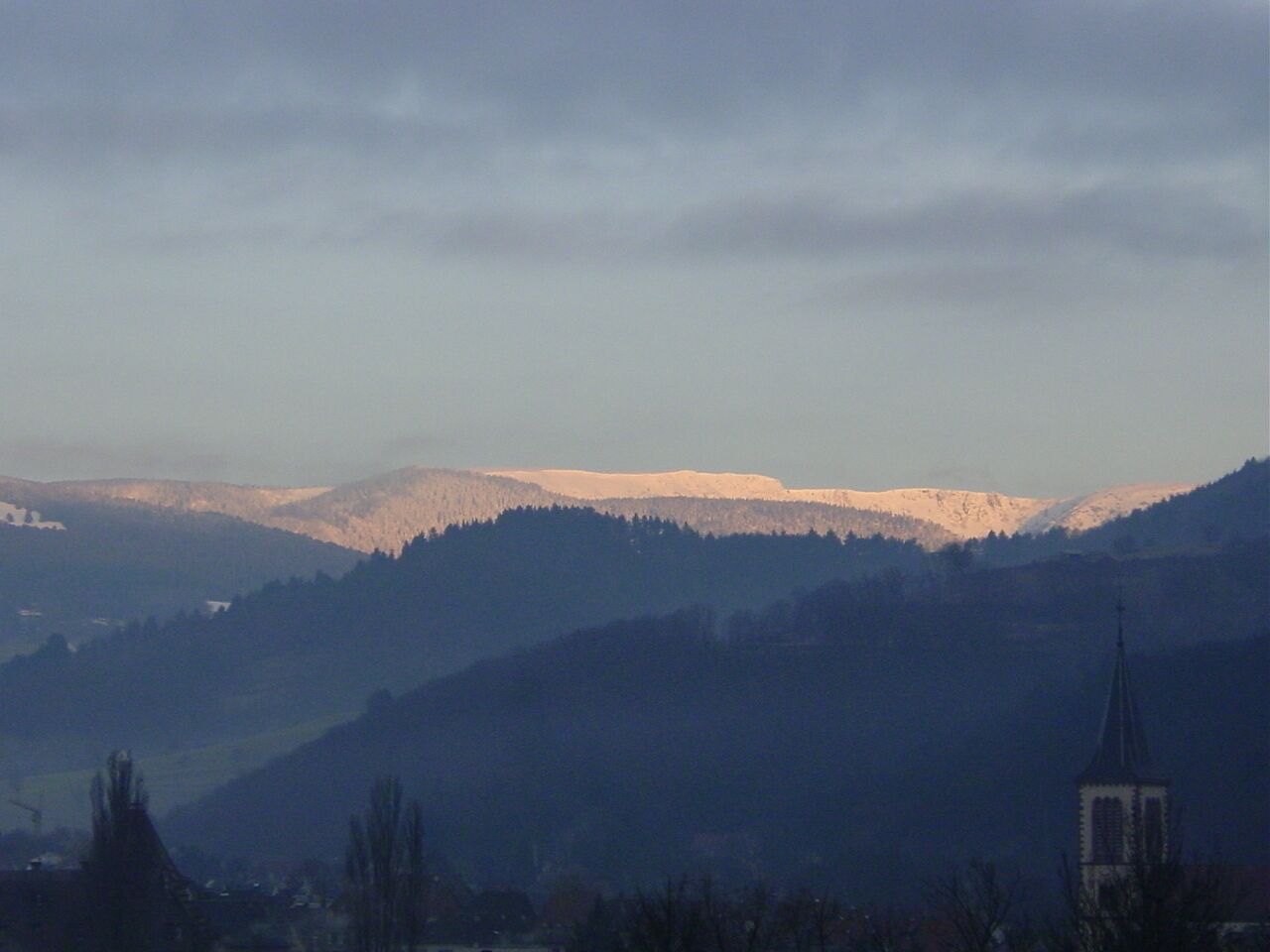 A mountainous landscape with a church spire in the foreground.