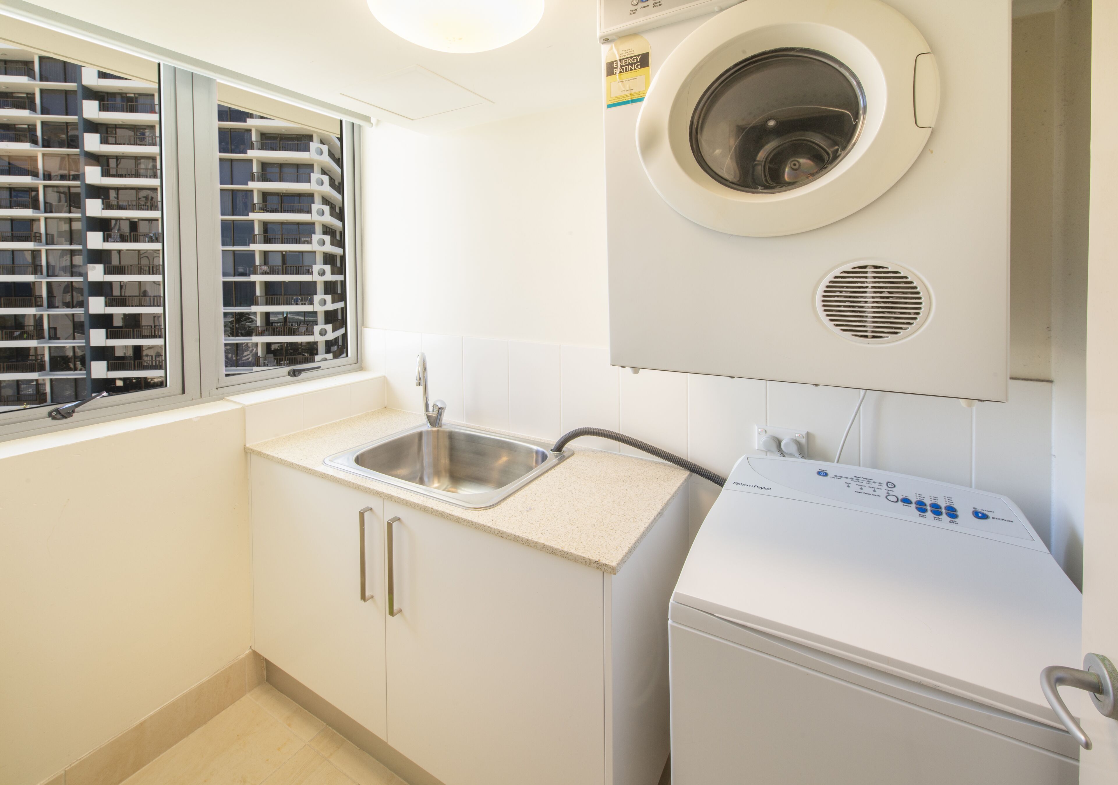 A laundry area with a washing machine, a sink, and a window with blinds.