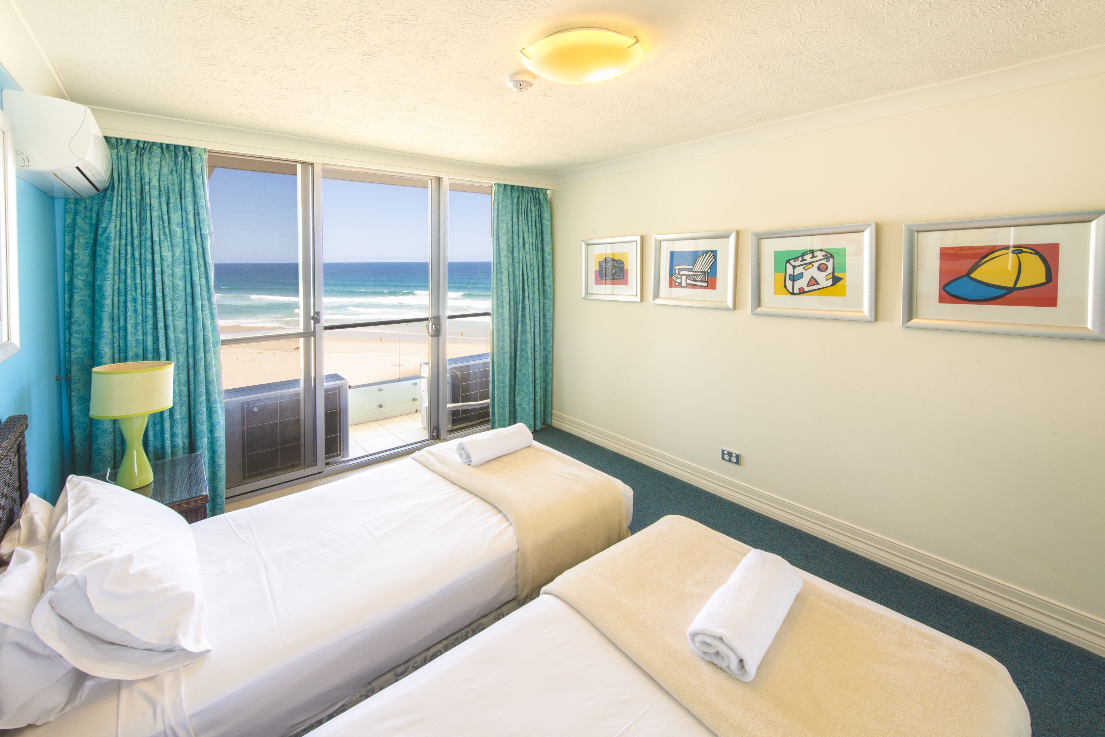 Ein Hotelzimmer mit zwei Betten, Blick auf den Strand und vier gerahmten Kunstwerken an der Wand.
