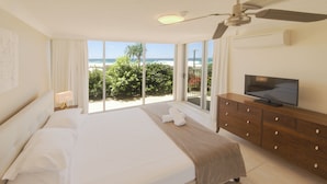 Ein Hotelzimmer mit Bett, Fernseher, Kommode und einem Balkon mit Blick auf den Strand.