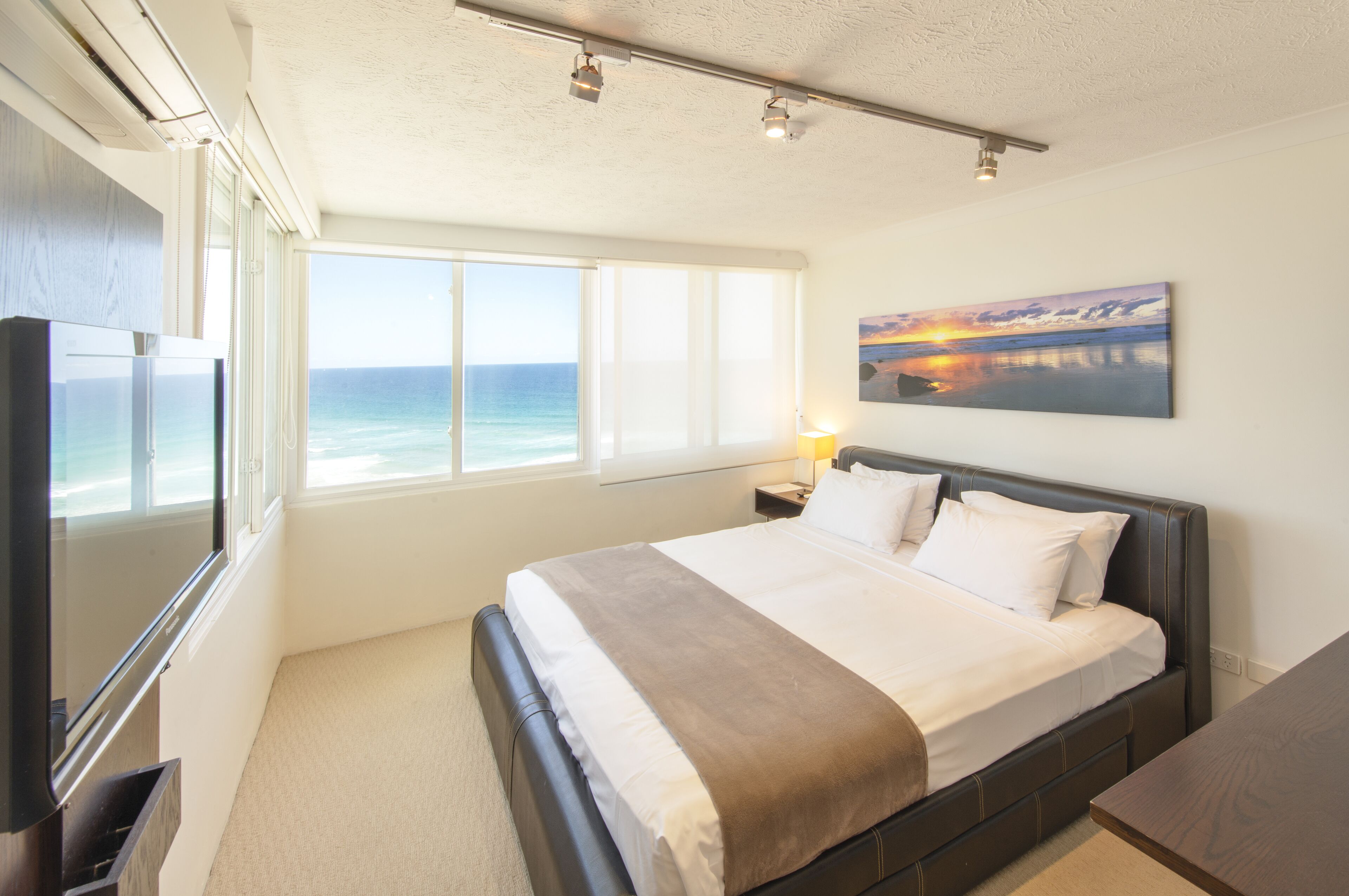 Ein Schlafzimmer mit einem großen Bett, einem Fernseher, einem Gemälde und Blick aufs Meer.