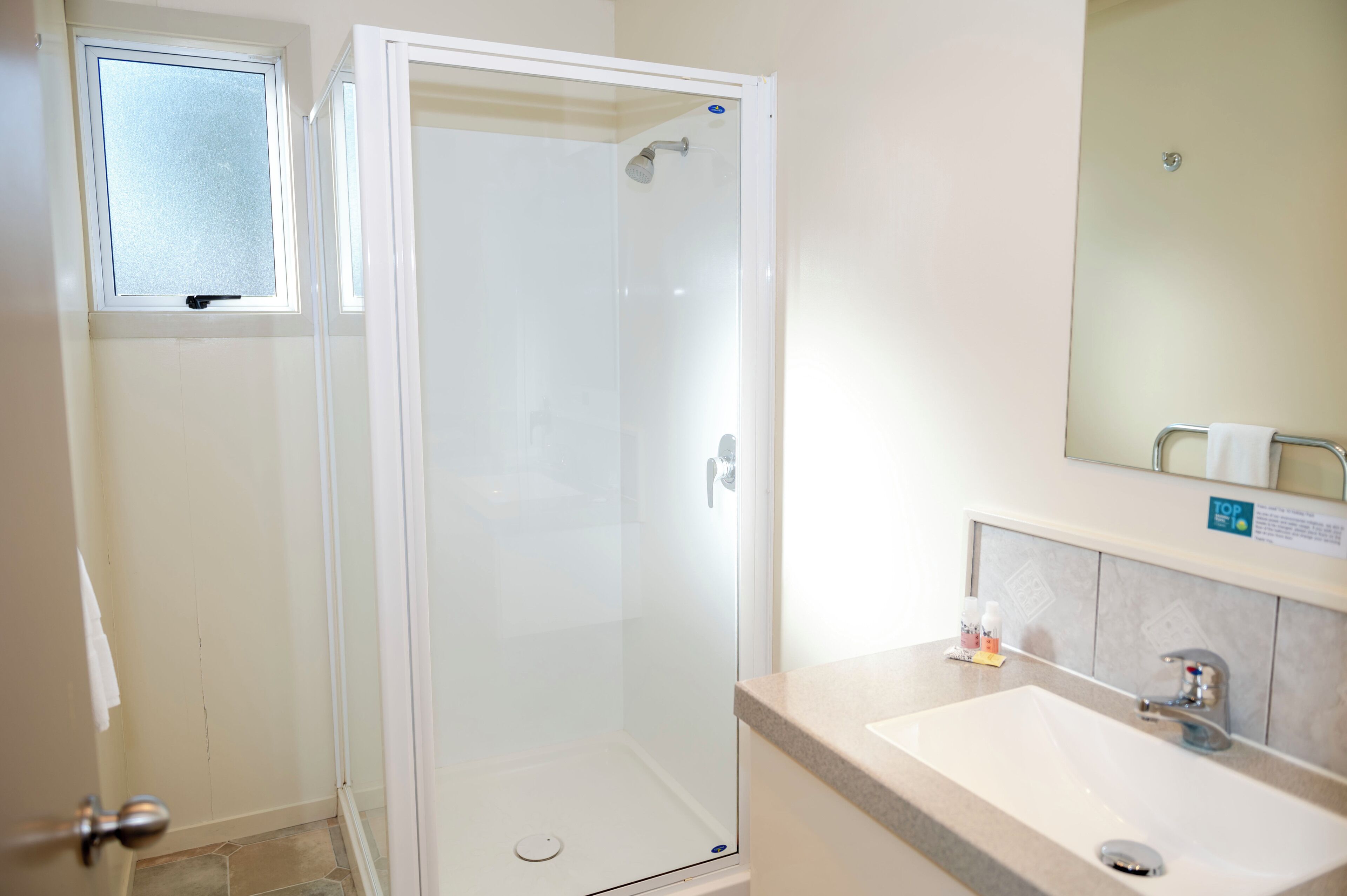 A bathroom with a glass-enclosed shower, a sink, and a mirror.