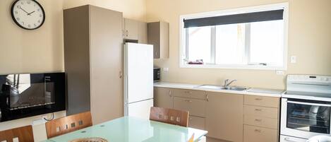 Cocina compacta con comedor, refrigerador, microondas, lavamanos y ventana con vistas.