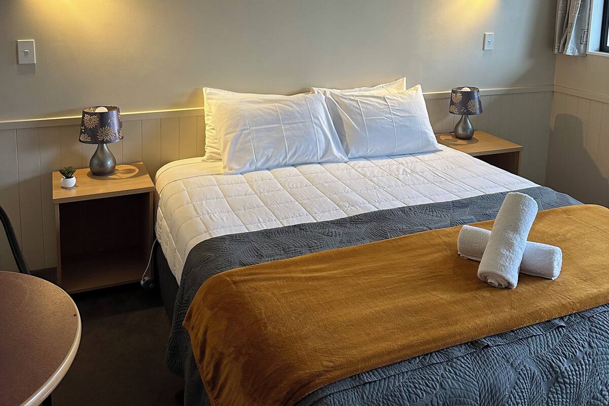 Habitación de hotel con cama, dos mesitas de noche, una lámpara y ventana con cortinas.