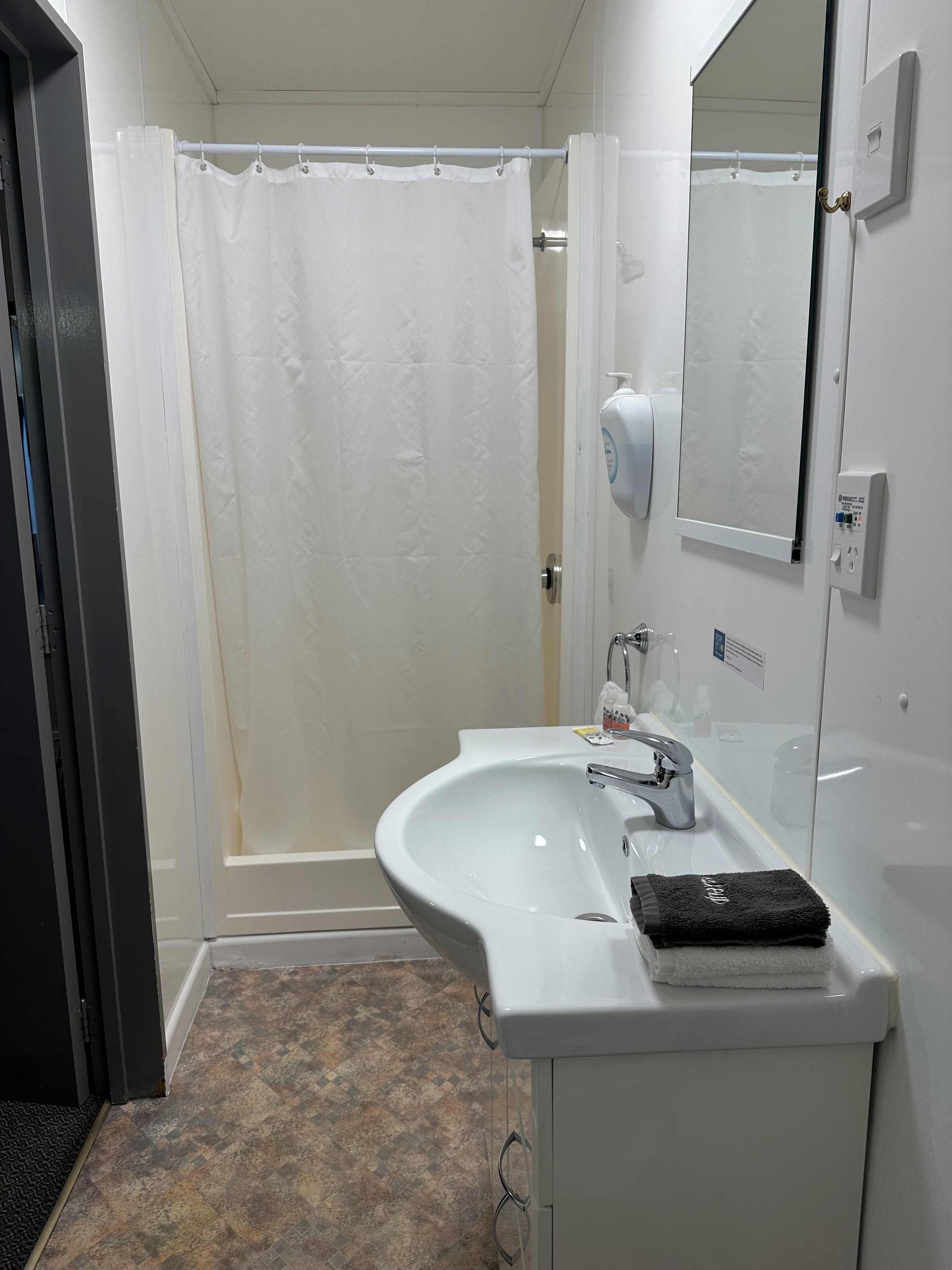 Un baño con un lavabo blanco, un espejo, una cortina de ducha y una toalla sobre el lavabo.