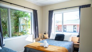 Hotellihuone, jossa on kaksi sänkyä, suuret ikkunat ja näkymä ulkona olevaan rakennukseen.