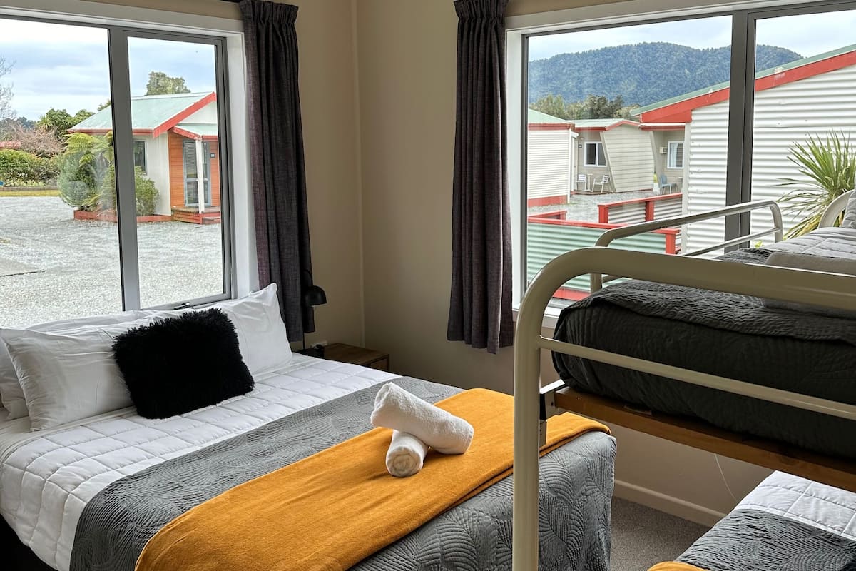 Habitación de hotel con dos camas, una ventana con cortinas y vista a un edificio y montañas.