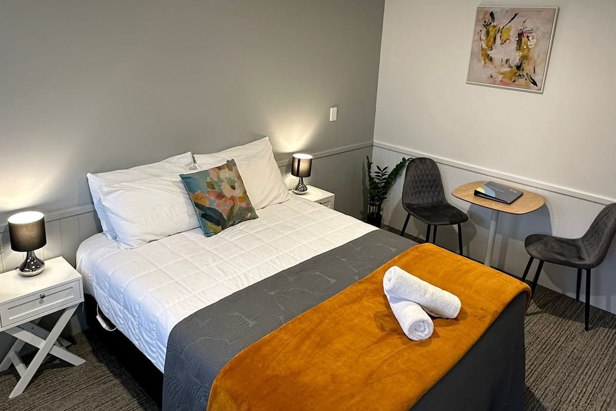 Una habitación de hotel con cama, mesitas de noche, escritorio, silla y un cuadro en la pared.