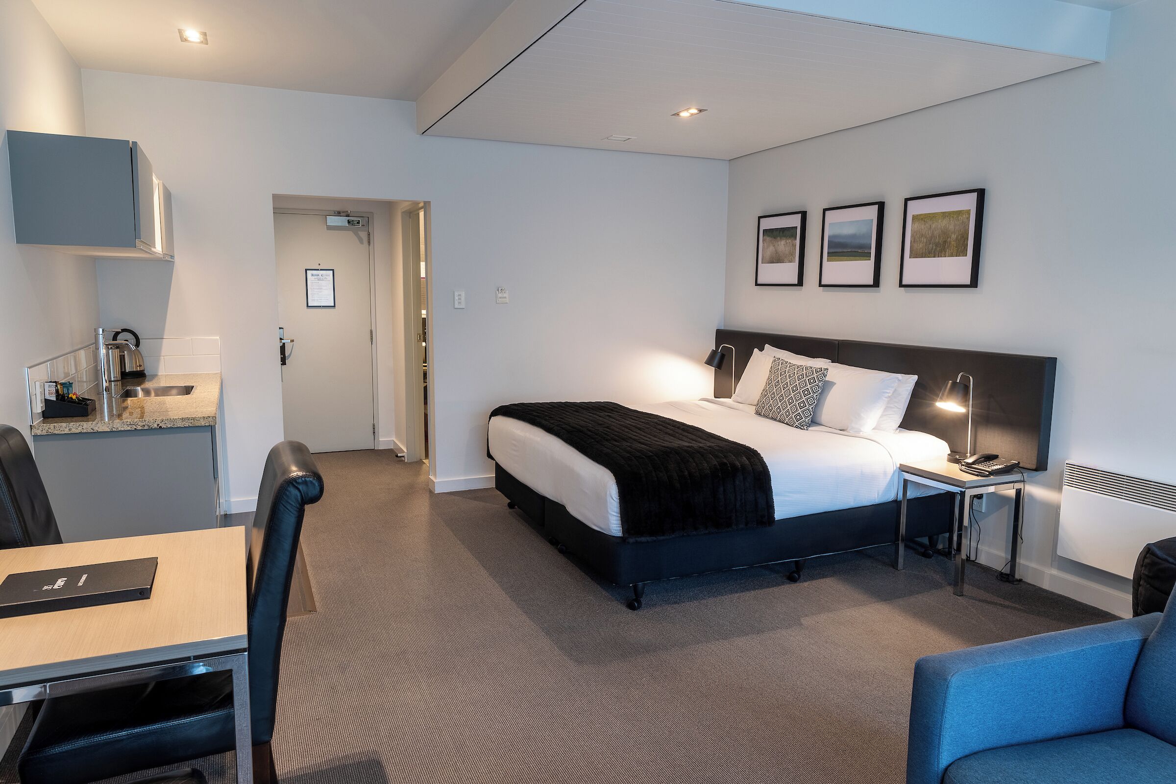 A modern hotel room with a bed, bedside table, lamp, and a desk with a chair.