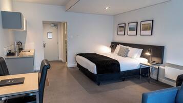 A modern hotel room with a bed, bedside table, lamp, and a desk with a chair.