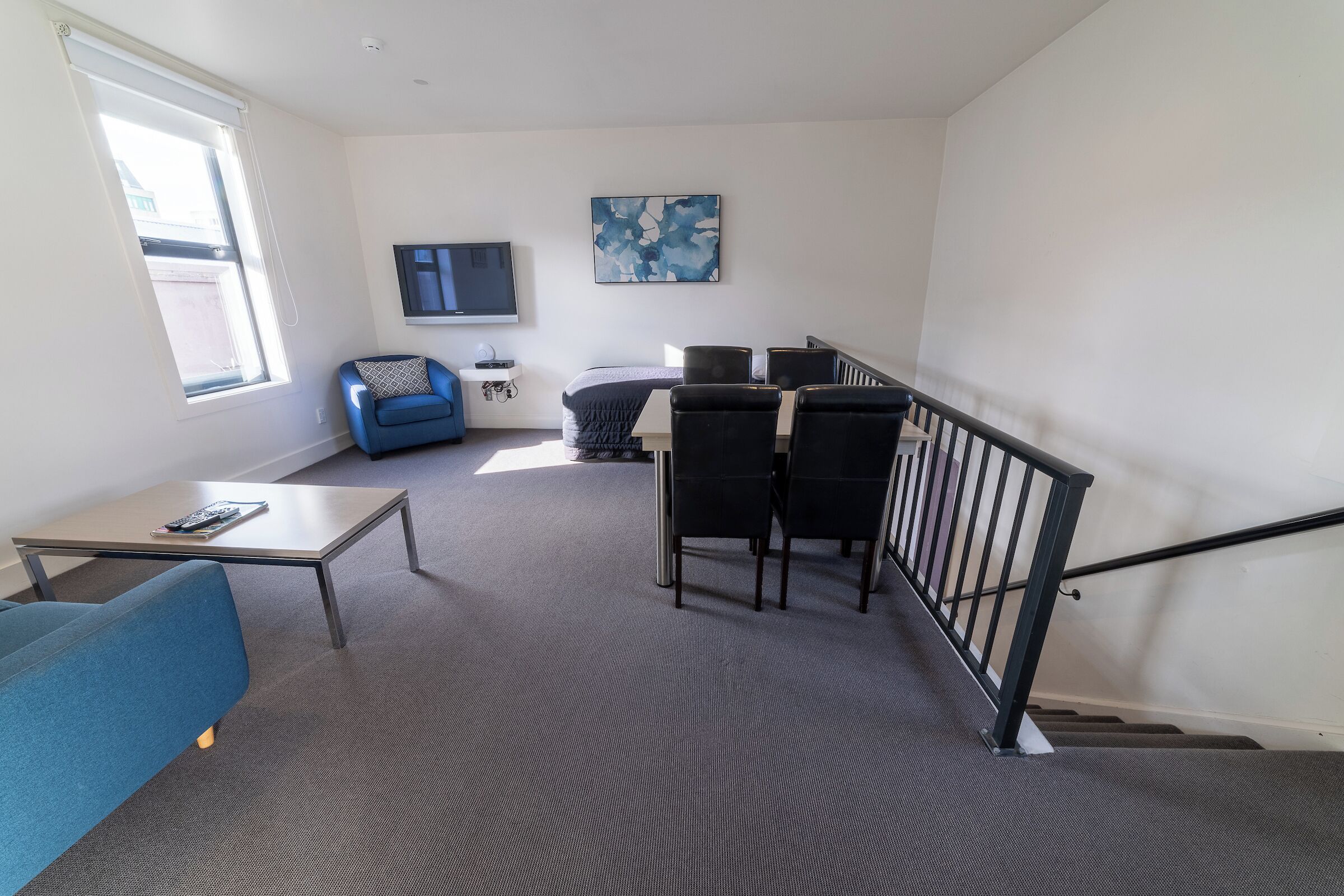 Un salon moderne avec un canapé bleu, une petite table, un téléviseur et un escalier.