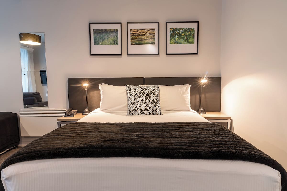 A neatly arranged hotel room with a large bed, bedside lamps, a bedside table with a phone, and three framed pictures on the wall.