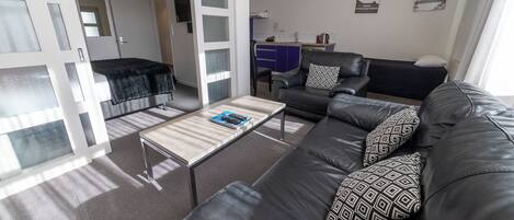 A modern living room with a sofa, a coffee table, and a kitchen area in the background.