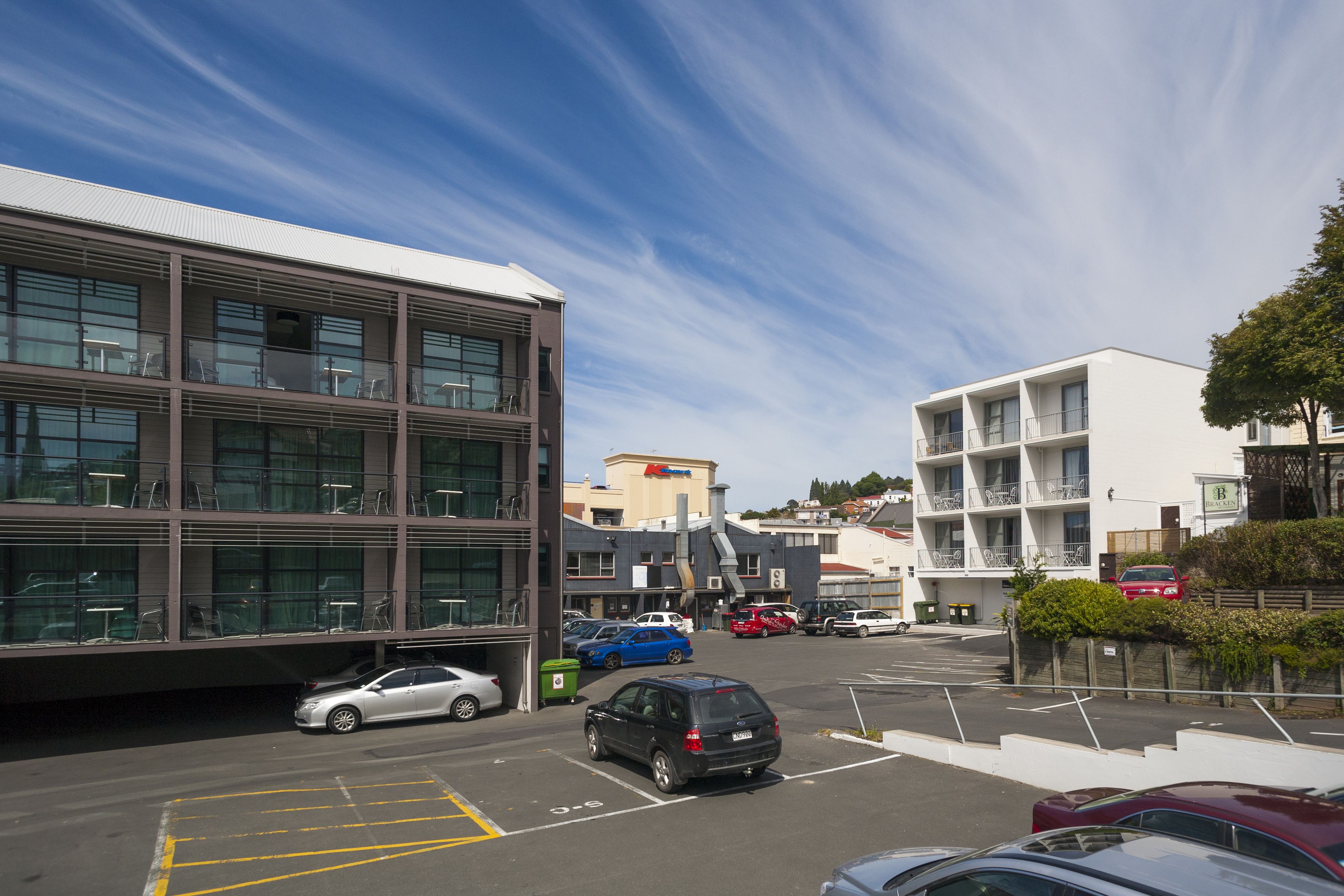 A parking lot with several cars, a building with multiple floors and balconies, and a clear sky.