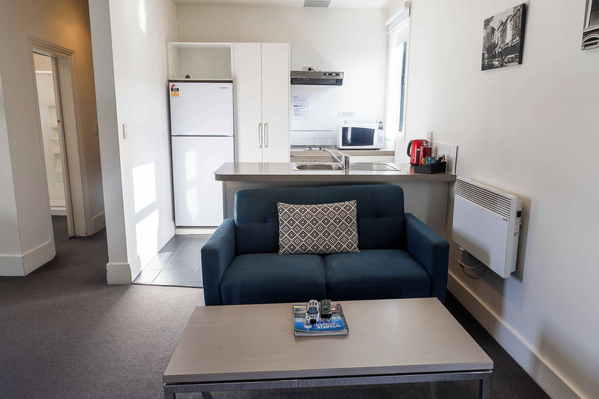 A compact living space with a kitchenette, a sofa with a patterned cushion, and a coffee table with a magazine.