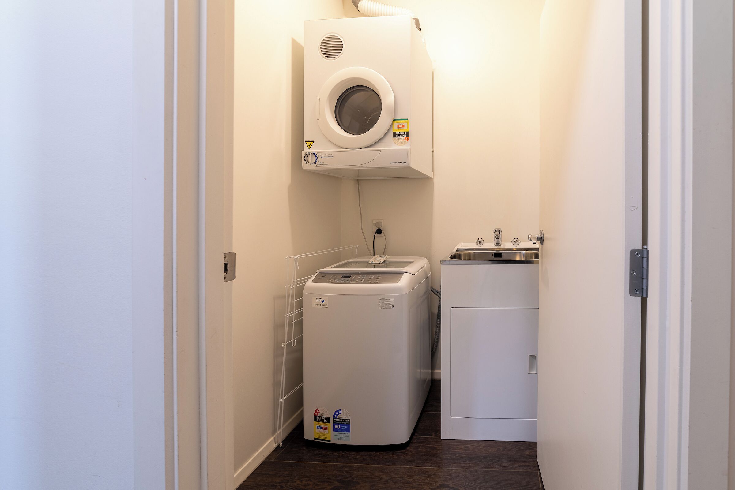 Ein Waschraum mit einer Frontlader-Waschmaschine und einem Trockner, einem kleinen Waschbecken und einer Lüftungsanlage über der Waschmaschine.