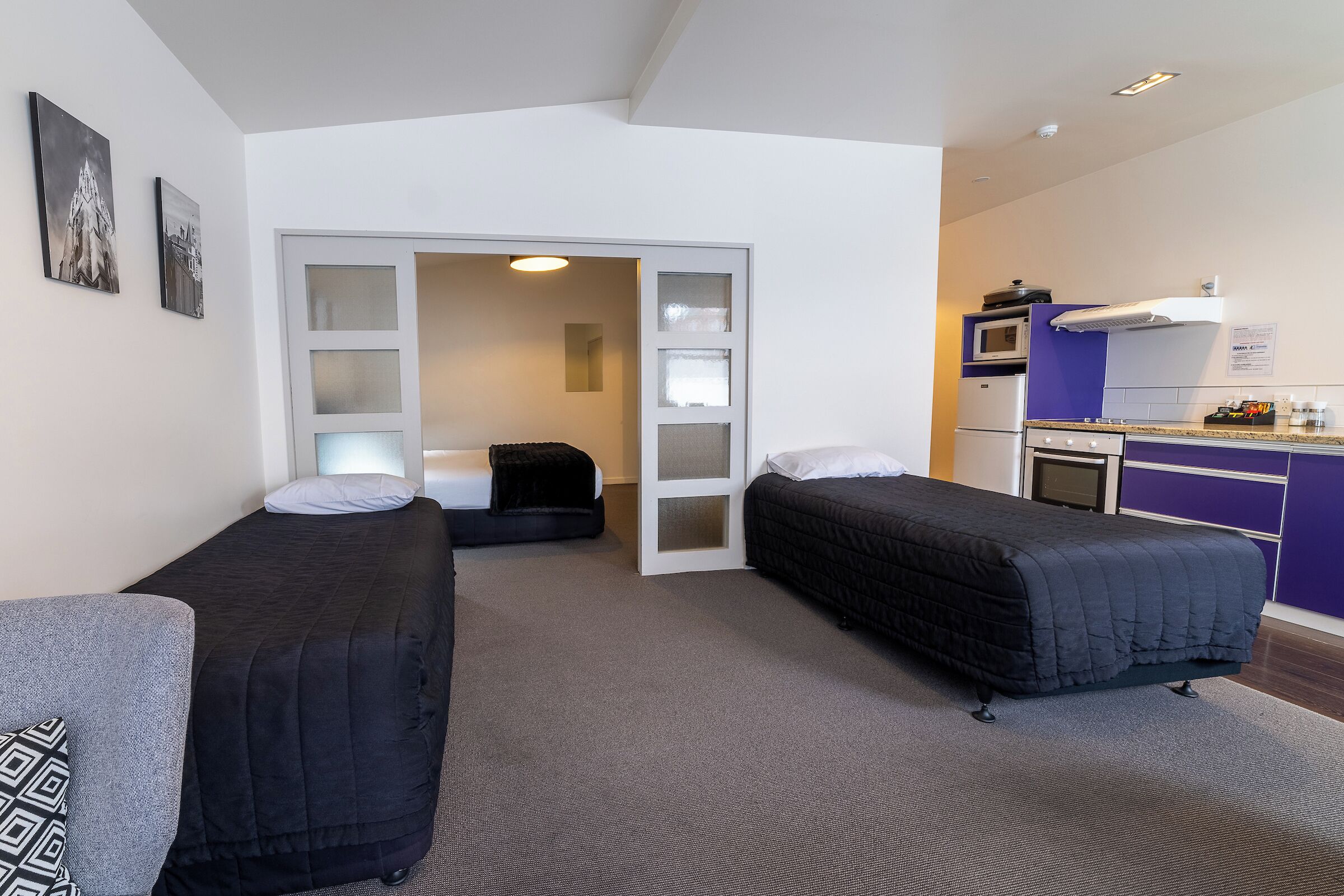 Ein kleines Zimmer mit zwei Einzelbetten, einer Küchenzeile und einer Tür zum Badezimmer.