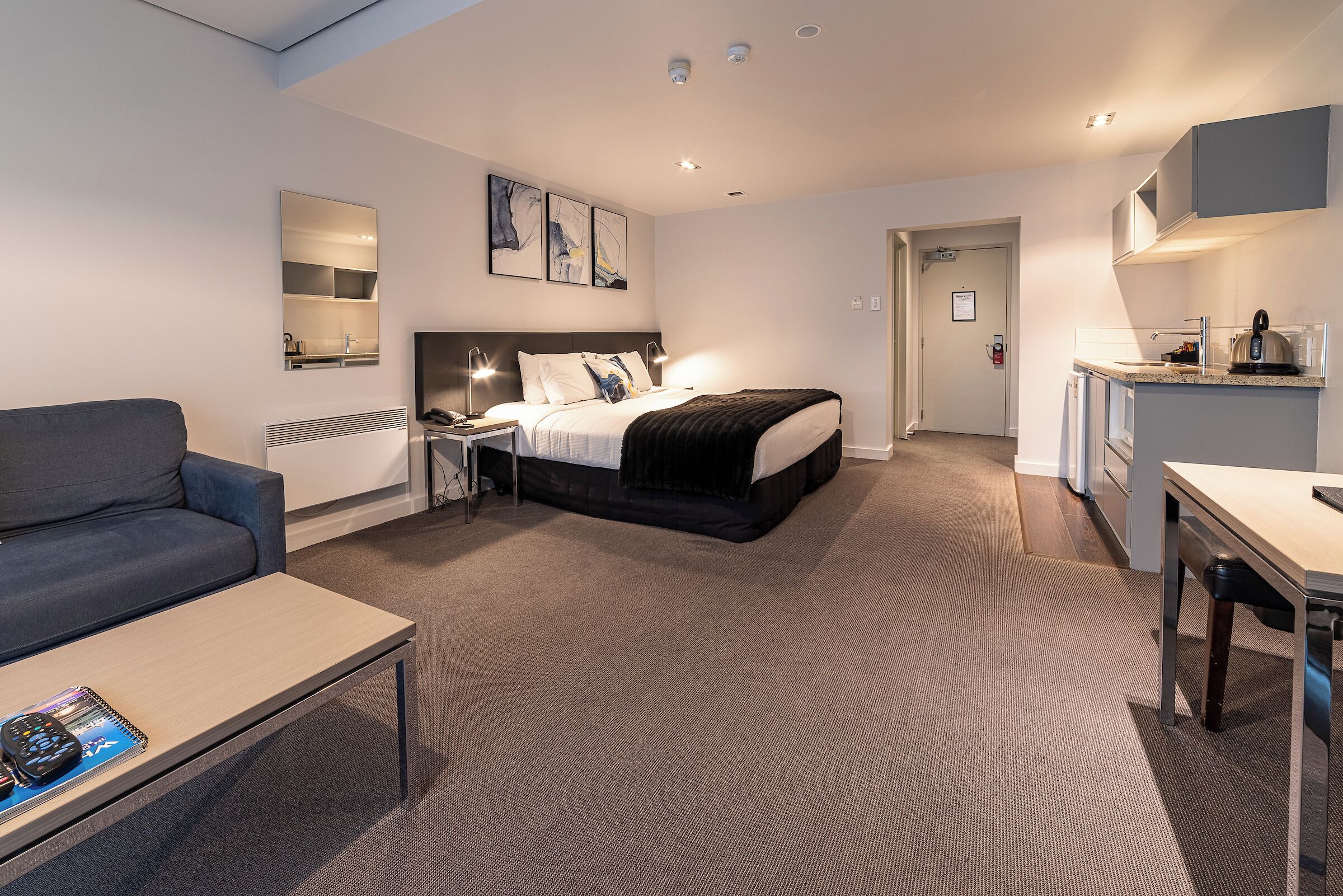Quarto de hotel com cama, sofá, escrivaninha, cozinha compacta e banheiro.