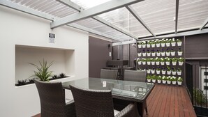 A glass-top table with wicker chairs, a wall-mounted planter with flowers, and a brick floor. - 315 Euro Motel & Serviced Apartments (Dunedin)