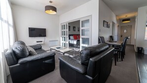 A modern living room with a black leather sofa, a flat-screen TV, and a dining area with a table and chairs. - 315 Euro Motel & Serviced Apartments (Dunedin)