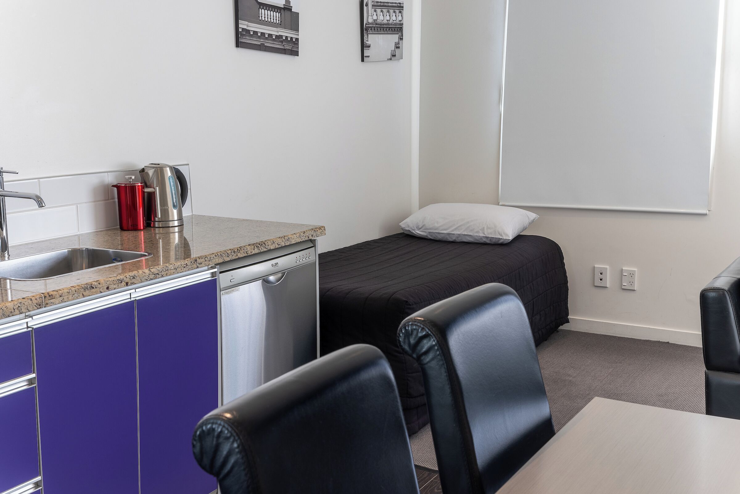 Habitació d'hotel petita amb cuineta, un llit, escriptori i una cadira.