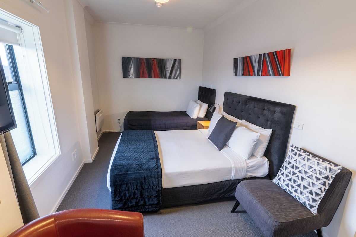 A hotel room with a large bed, a smaller bed, a sofa, and a TV.