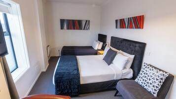 Une chambre d’hôtel avec un grand lit, un lit plus petit, un canapé et une télévision.