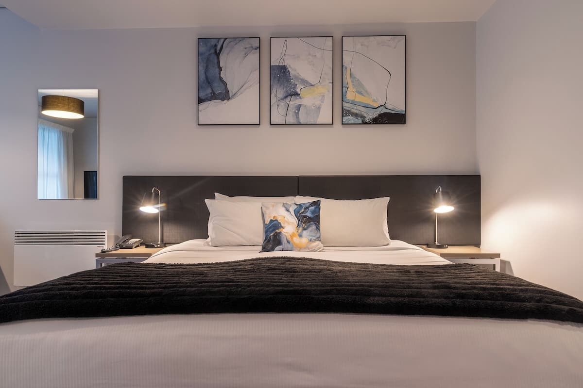 A modern bedroom with a large bed, two bedside lamps, and abstract wall art.