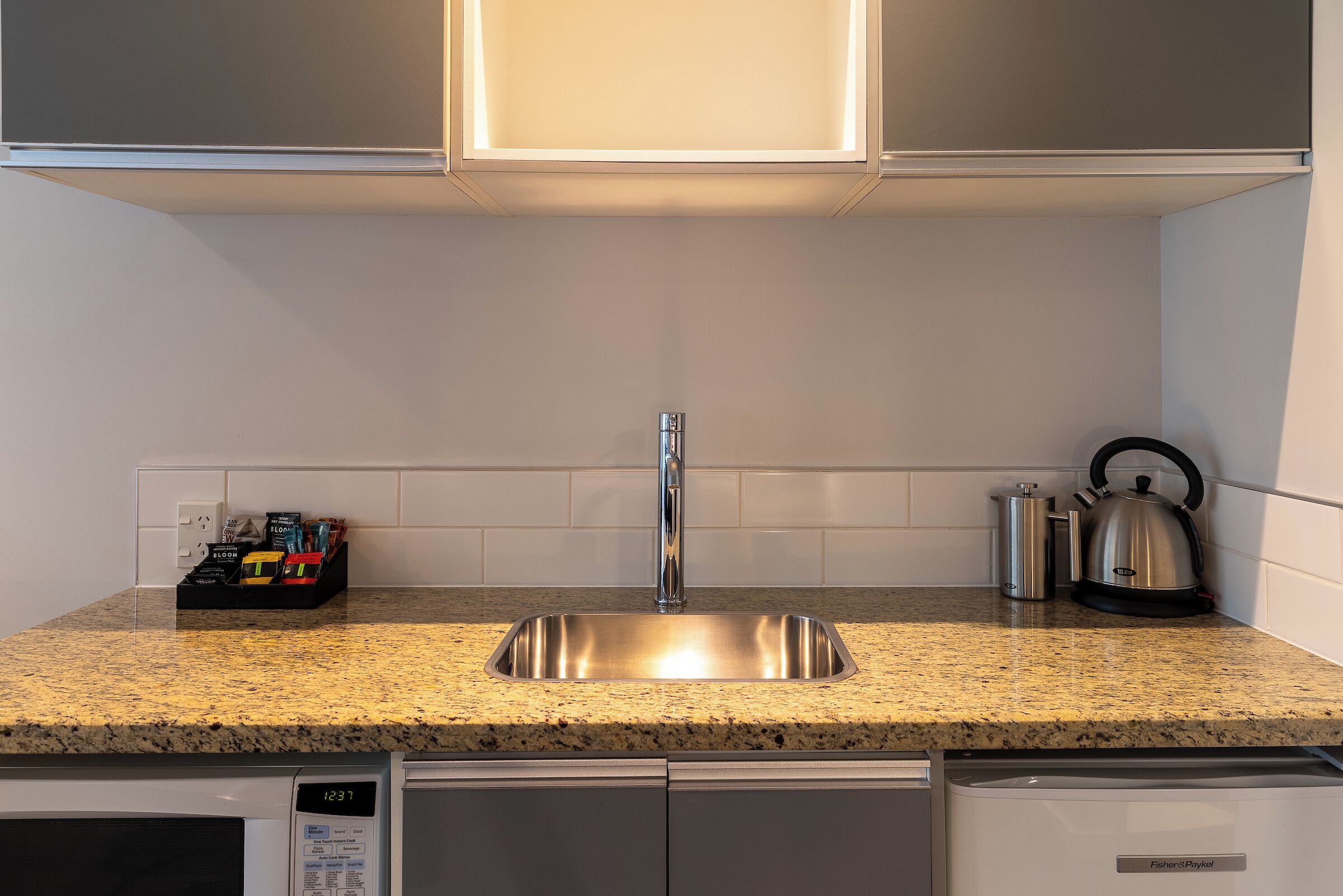 Una cocina con encimera de granito, pileta de acero inoxidable y hervidor.