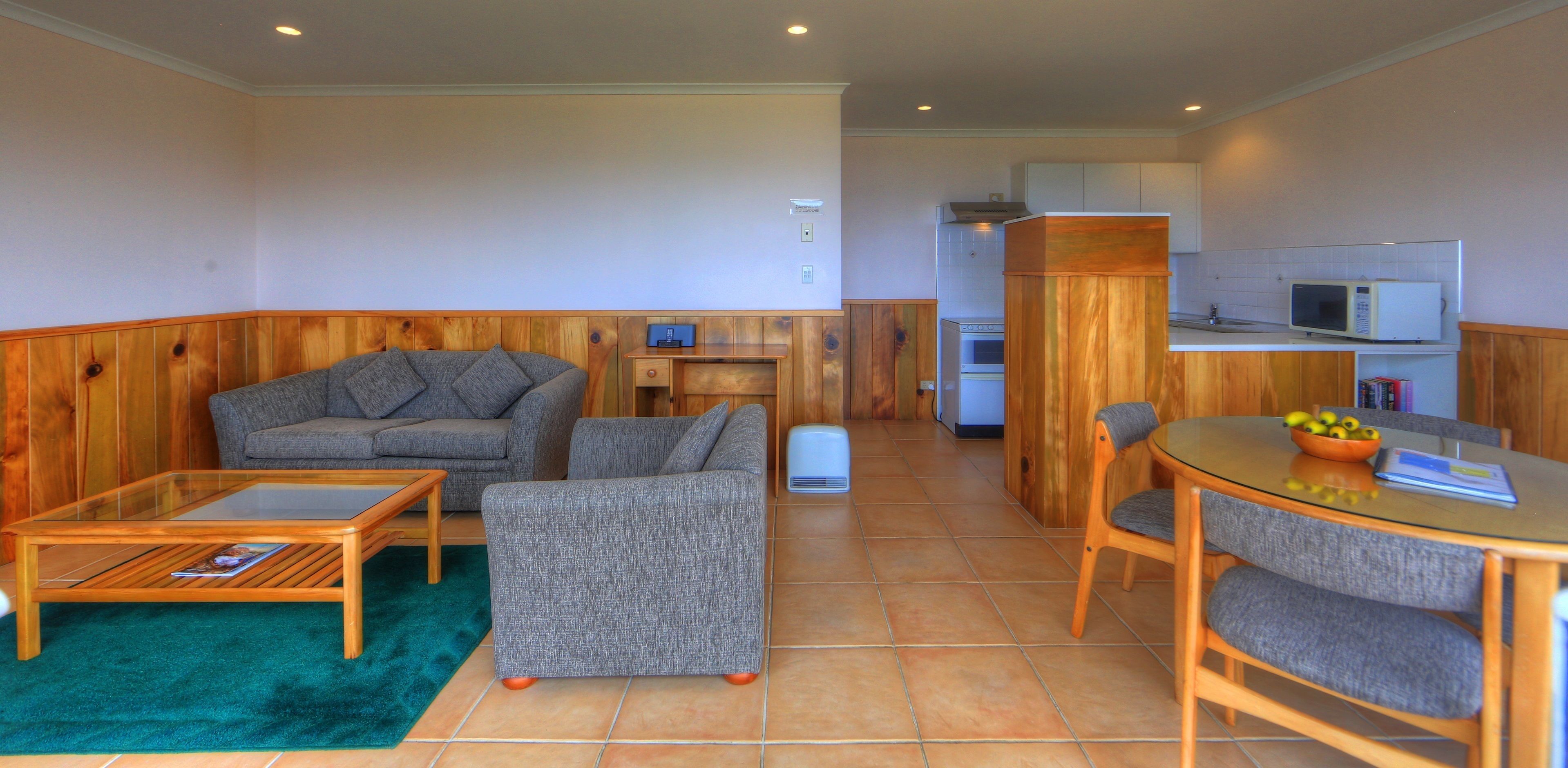A compact living space with a sofa, a coffee table, a dining table with chairs, a microwave, and a small kitchen area.