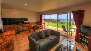 A living room with a sofa, TV, and a view of the sea. - Islander Lodge Apartments (Norfolk Island)