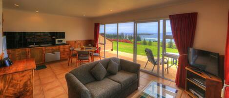 A living room with a sofa, TV, and a view of the sea.