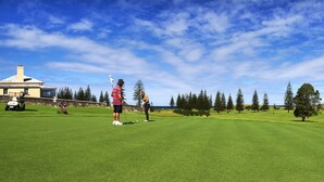 A golf course with a clubhouse, trees, and a clear sky. - Islander Lodge Apartments (Norfolk Island)