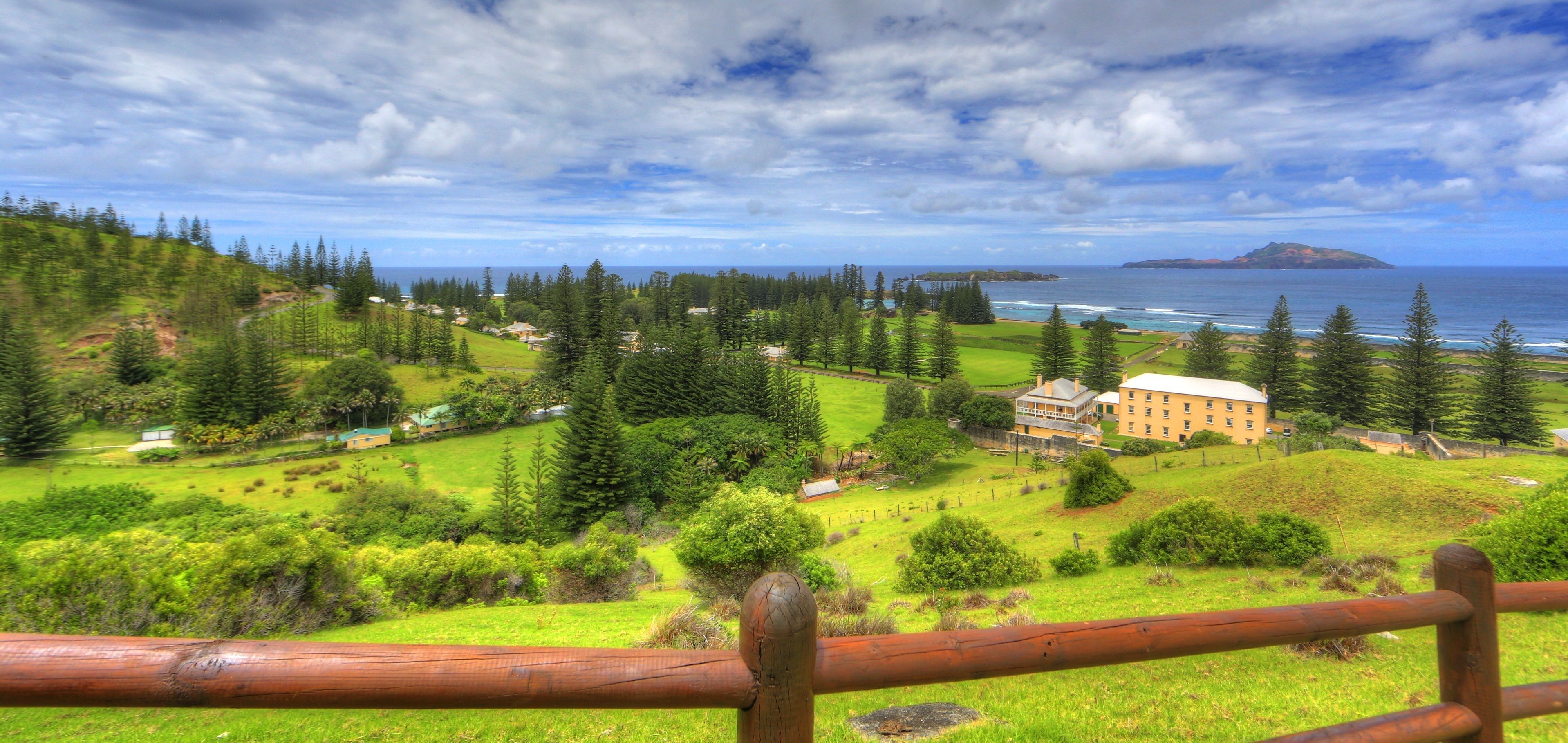 A coastal landscape with a prominent building surrounded by lush greenery and a view of the ocean.