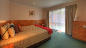 A hotel room with a bed, a nightstand, a dresser, a window with curtains, and a framed picture on the wall. - Islander Lodge Apartments (Norfolk Island)