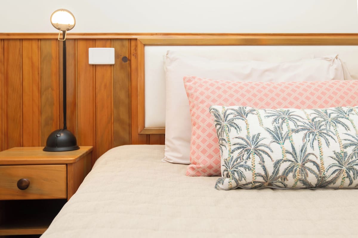 A neatly made bed with a patterned pillow, a bedside lamp, and a wooden nightstand with a drawer.