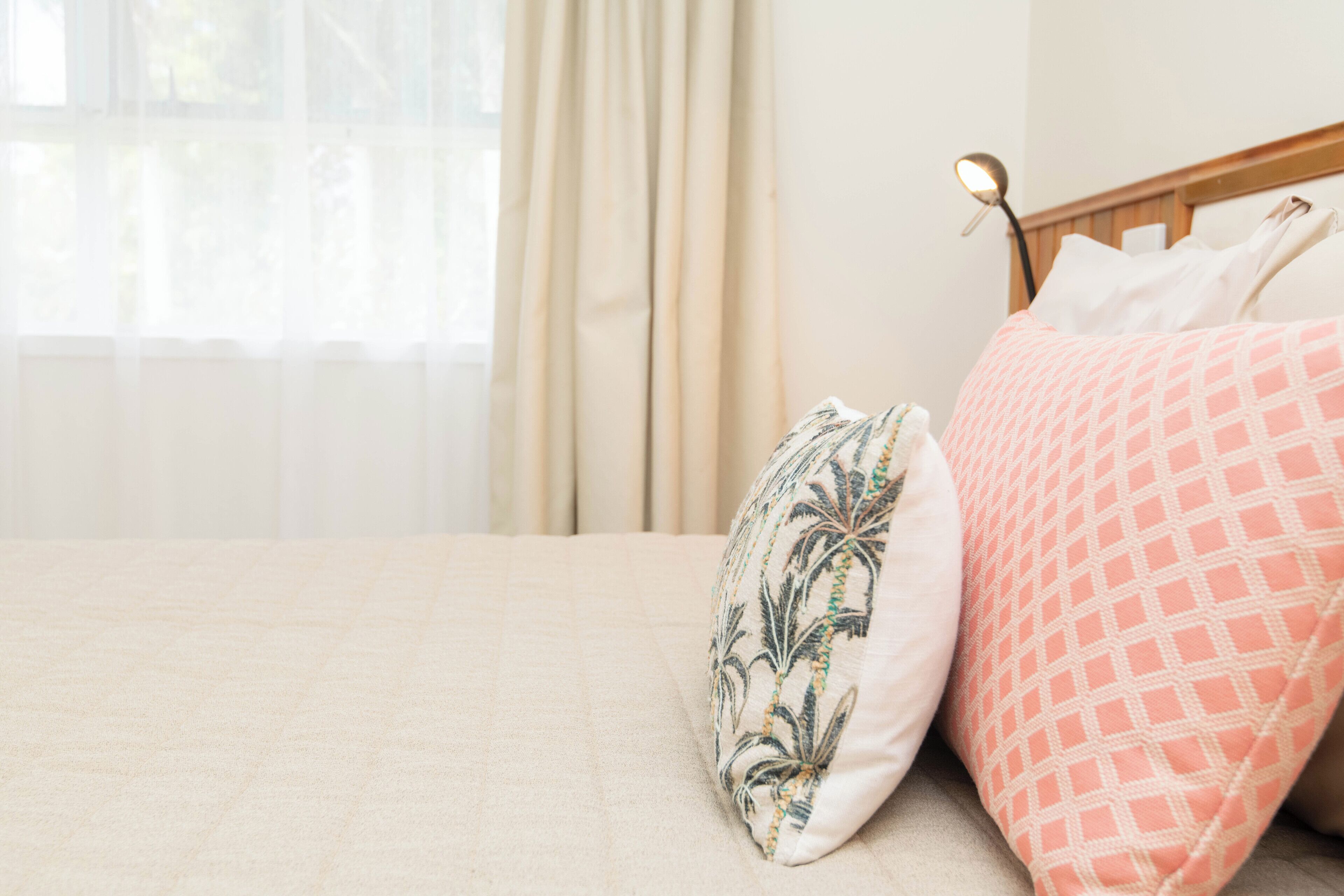 Un lit avec une couvre-lit beige, un coussin à motifs et un coussin rose orné d’un motif géométrique.