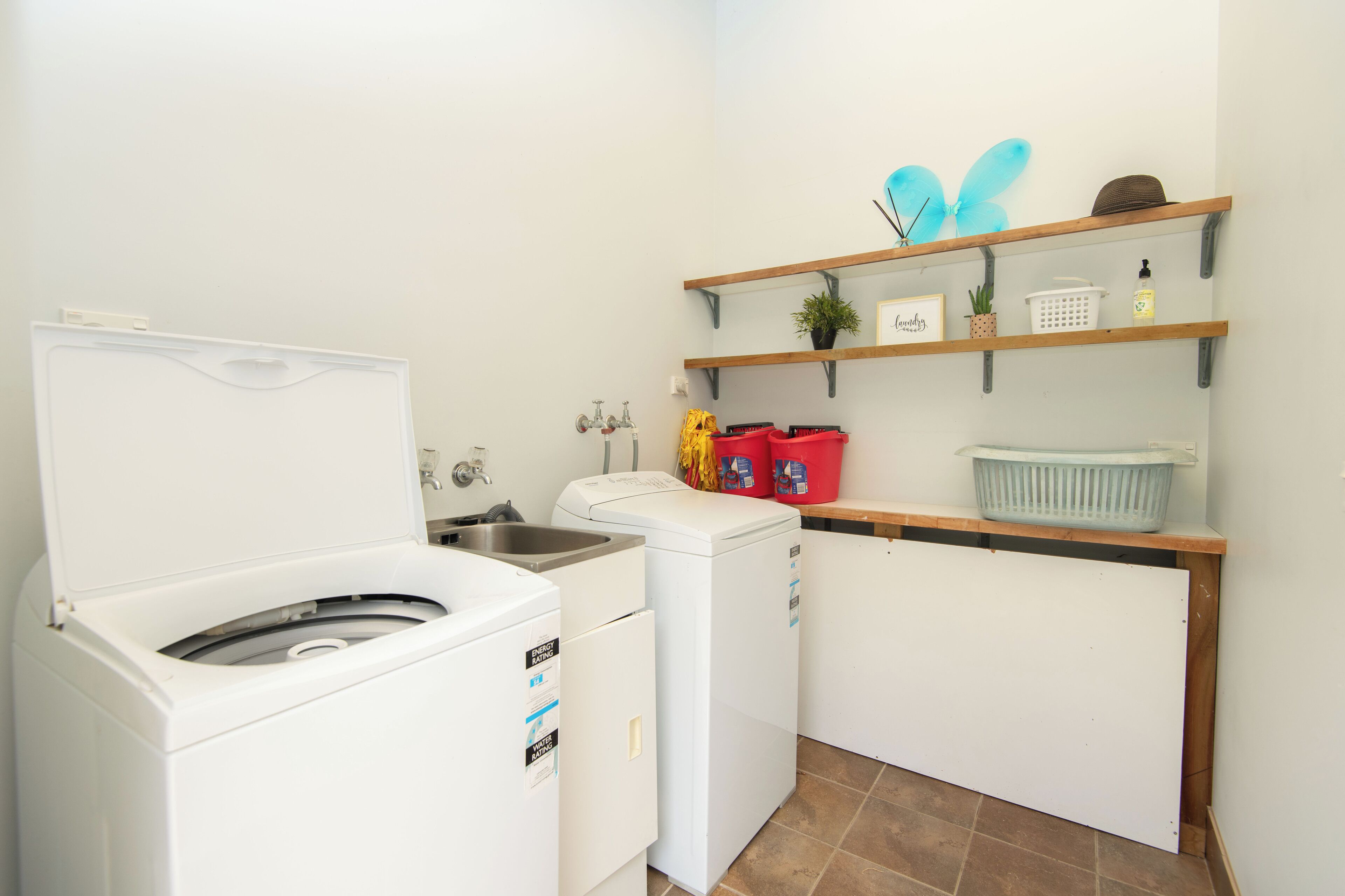 A compact kitchen with a washing machine, a small refrigerator, and wooden shelves above holding various items.