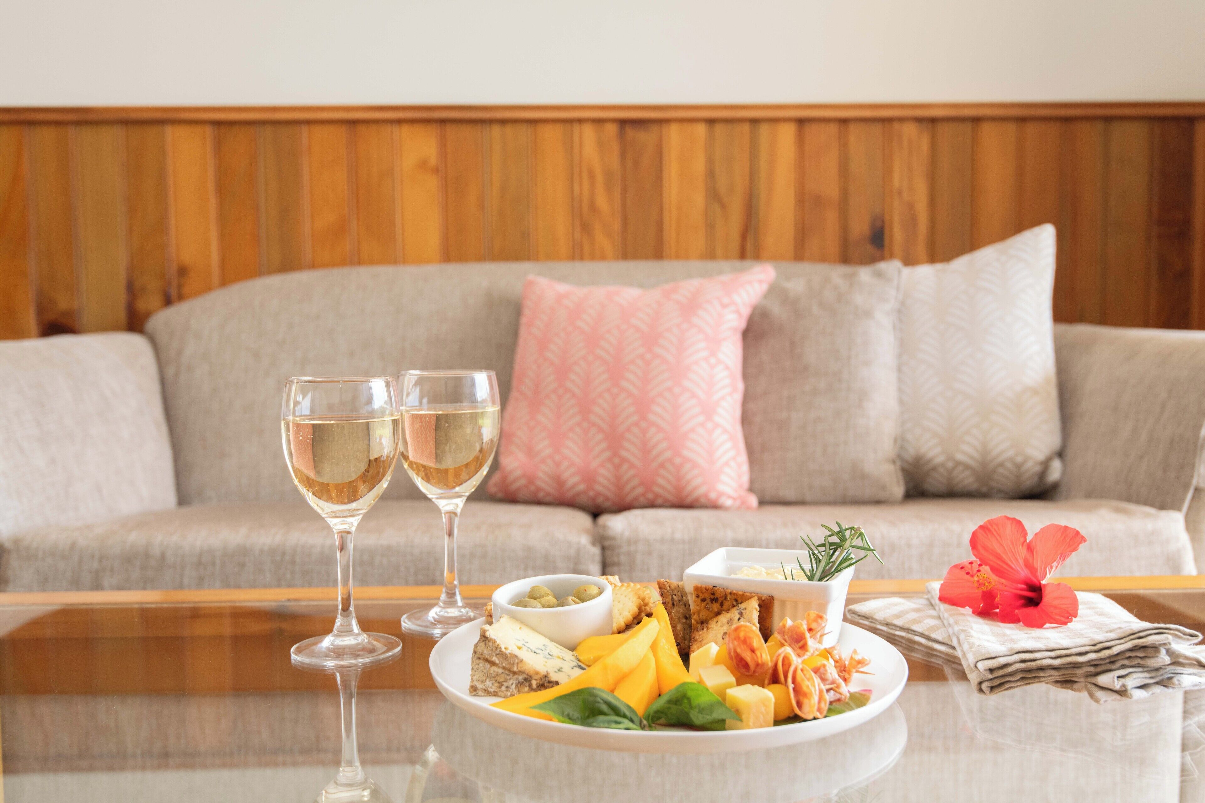 Une table à manger avec une assiette de nourriture, deux verres de vin blanc et une fleur d’hibiscus.