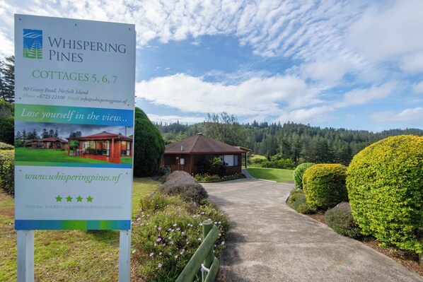 A sign for Whispering Pines Cottages 5, 6, 7, including contact information and a website URL. - Whispering Pines (Norfolk Island)